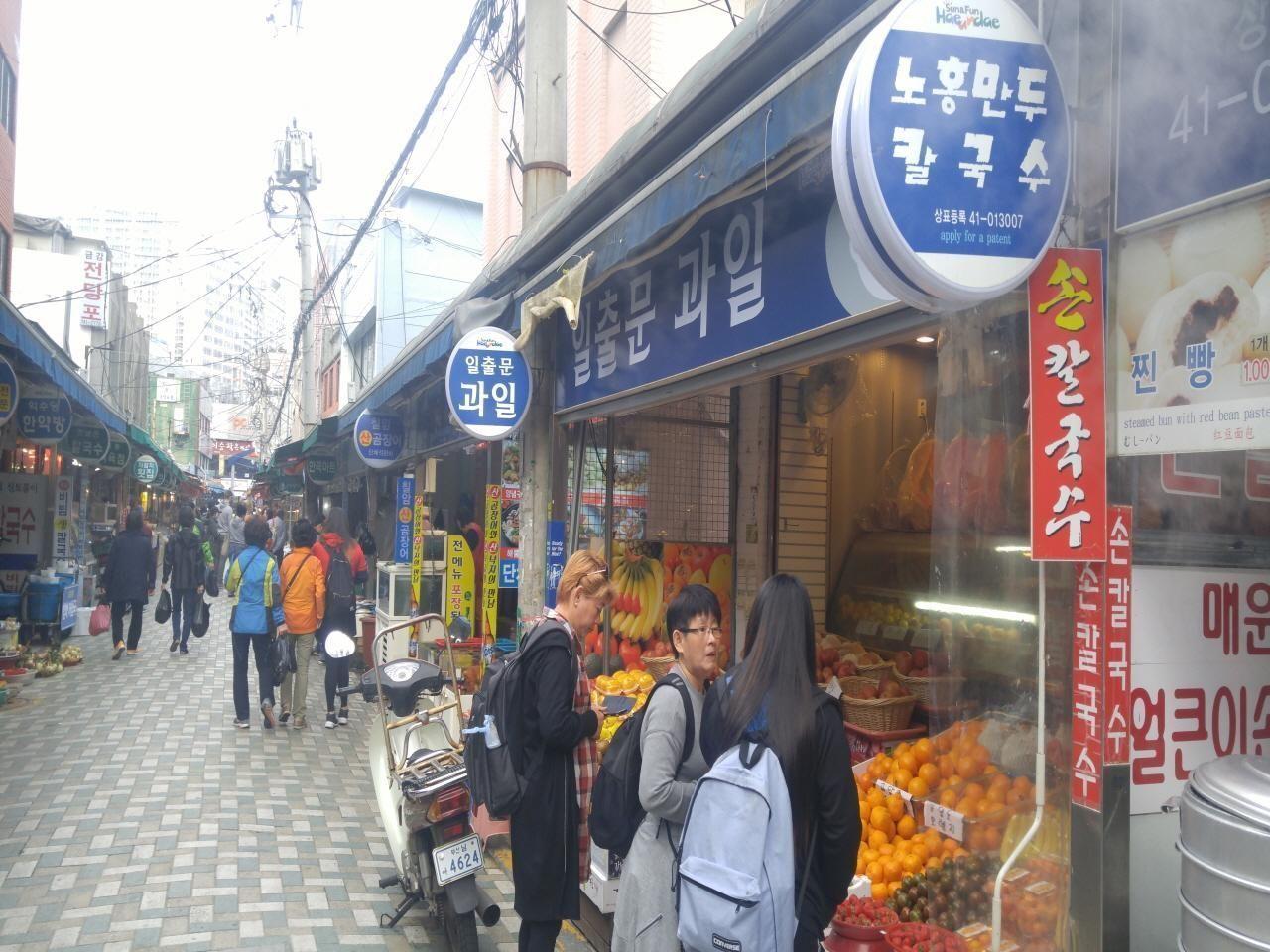 Bustling alleyway in Haeundae Market, Busan, lined with stalls selling fresh produce and local snacks.
